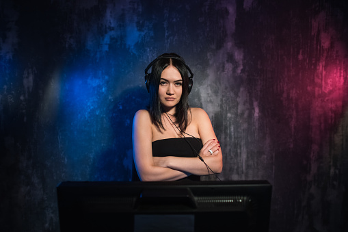 A woman looks at camera while sitting in front of her PC and playing online computer games and streaming game on the internet. Gamer girl plays at the table in his room