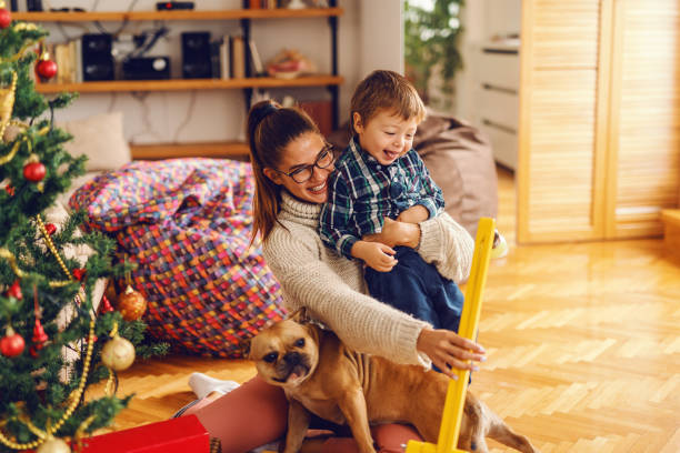 istock Young mom holding dog in lap while playing with son. Next to them Christmas tree. Home interior, Christmas holidays concept. 1077731144