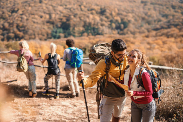 istock Cute couple looking at map while their friends in background looking at view. Hiking concept. 1077733766