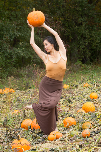 Adult woman dancer dressed in earth tones, dancing in a farm field while holding a pumpkin, in Ellington, Connecticut.