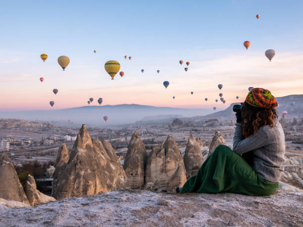 Young girl is shooting photos of hot air balloons flying in red and rose valley in Goreme in Cappadocia in Turkey Cappadocia, Hot Air Balloon, Photographer, Famous Place, Turkey - Middle East rock hoodoo stock pictures, royalty-free photos & images