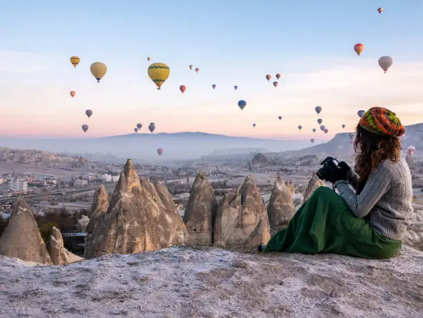Photo of Young girl is shooting photos of hot air balloons flying in red and rose valley in Goreme in Cappadocia in Turkey
