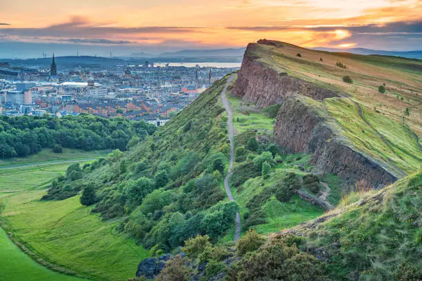Stock photograph of Salisbury Crags in Holyrood Park and downtown Edinburgh Scotland UK during sunset