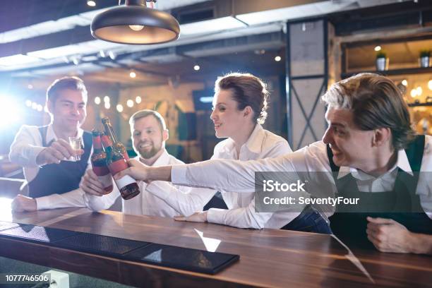 Excited Restaurant Colleagues Clinking Beer Bottles At Bar Count Stock Photo - Download Image Now