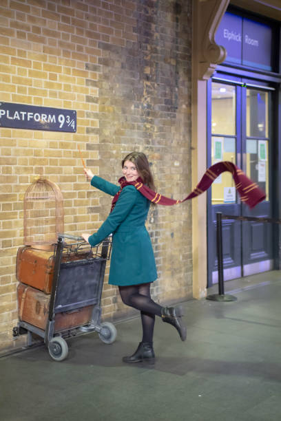 Harry Potter's platform 9 3/4 at Kings Cross London with a young woman Harry Potter fan having a photo taken wearing a Hogwarts scarf and pushing the trolley into the wall.