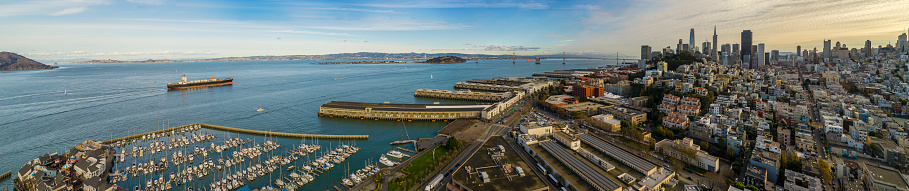 Remote aerial panoramic view of San Francisco Downtown over the residential areas and piers at sunset. The skyline includes the major buildings Salesforce Tower, Transamerica Pyramid, Lumina, Coit Tower, and more. Northern California, USA. extra-wide stitched panorama