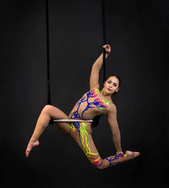 A young girl performs the acrobatic elements in the air trapeze. Studio shooting performances on a black background.