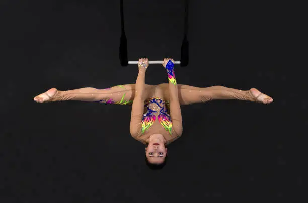 A young girl performs the acrobatic elements in the air trapeze. Studio shooting performances on a black background.