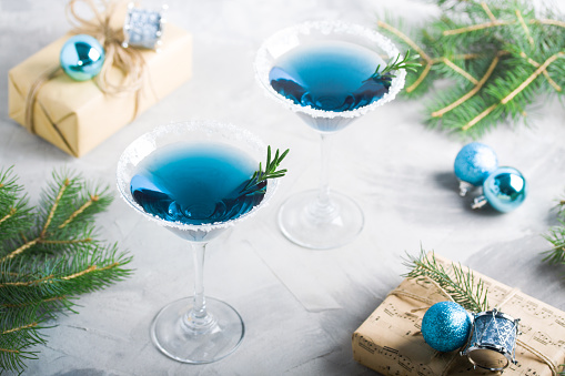 Christmas composition with martini drinks with rosemary and sugar decoration, fir-trees, balls, \n\ncraft gift boxes in blue colors, gray concrete background. Winter holiday, New Year party \n\nconcept.