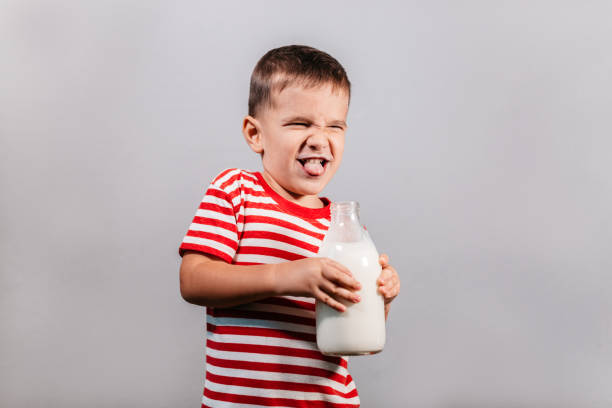 Child with bottle of milk against grey background. Portrait of young boy with milk mustache making faces isolated over gray background - studio shot. food elementary student healthy eating schoolboy stock pictures, royalty-free photos & images