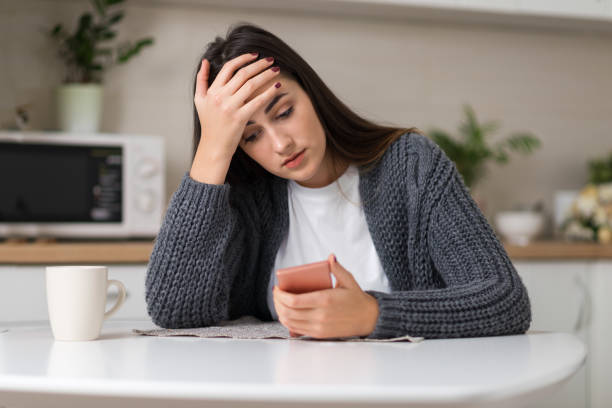 Depressed woman reading a text message on mobile phone Stressed woman reading something on her cell phone at home waiting telephone on the phone frustration stock pictures, royalty-free photos & images