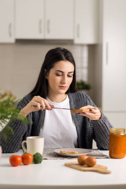istock Young woman spreading jam on a slice of bread 1077812934