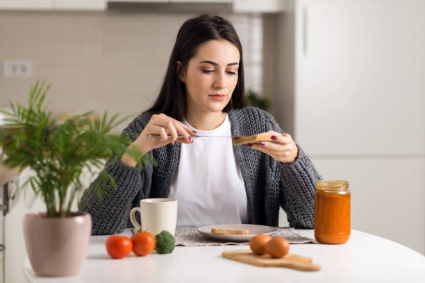 istock Young woman spreading jam on a slice of bread 1077813004