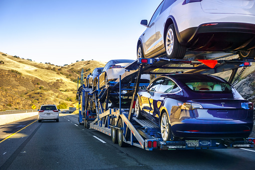 December 2, 2018 Gilroy / CA / USA - Car transporter carries Tesla Model 3 new vehicles along the highway, back view of the trailer