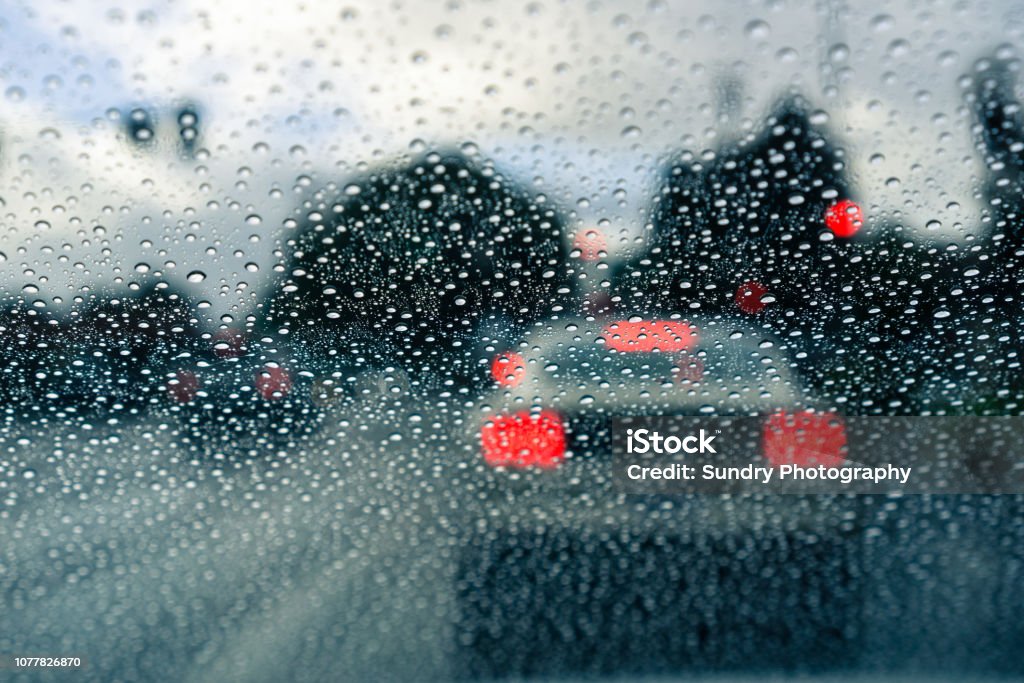 Raindrops on the windshield on a rainy day; car stopped at a traffic light in the background Raindrops on the windshield on a rainy day; blurred car stopped at a traffic light in the background; California Rain Stock Photo