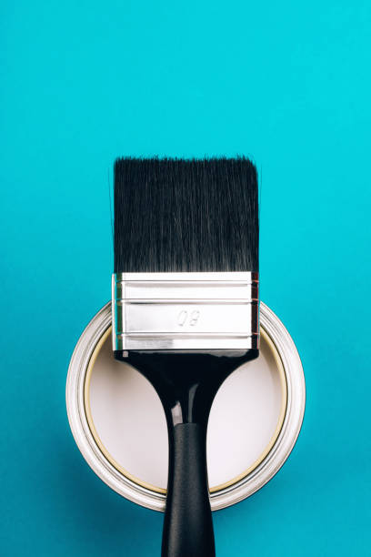 istock Brush with black handle on open can of white paint on blue background. 1077835432