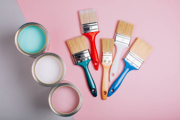 istock Three open cans of pastel paint with five brushes on pink and grey background. 1077835456