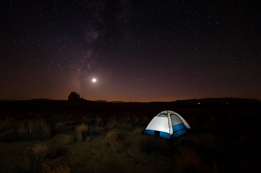 Lit tent in the desert with a mountain peak in the background during a clear night sky after sunset. Taken at Shiprock, New Mexico, United States.