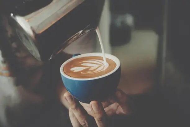Photo of Barista pouring milk in coffee cup for make latte art.