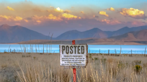 Posted sign against Utah Lake mountain and sky Posted sign against Utah Lake mountain and sky. Old Posted sign prohibiting people from trespassing on the grassy private property near Utah Lake with mountain under a cloudy sky in the background. lake utah stock pictures, royalty-free photos & images