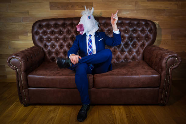 istock Funny unicorn in elegant suit siting on sofa 1077895738