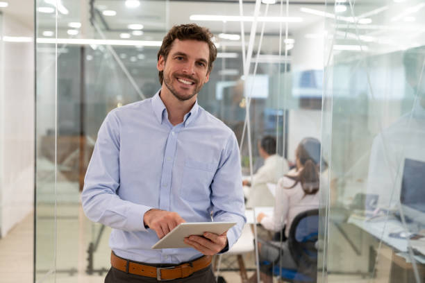 istock Latin american handsome businessman facing camera smiling while holding his tablet at the office 1077900726