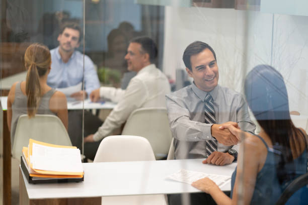 istock Business partners at the office handshaking looking happy while other people work at the background 1077900764