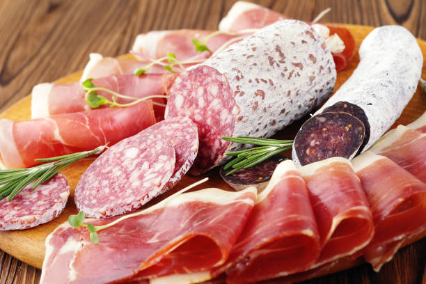 Delicias de carne de primer plano, lonchas finas de jamón y Salchicha italiana en una tabla de madera. - foto de stock