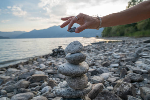 dettaglio della persona che impila rocce in riva al lago - perfection nature balance stone foto e immagini stock