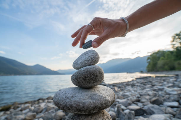dettaglio della persona che impila rocce in riva al lago - perfection nature balance stone foto e immagini stock
