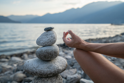 Detail of person exercising yoga and meditation near stack rock by the lake at sunset, shot in Ticino Canton, Switzerland.
People life balance concept