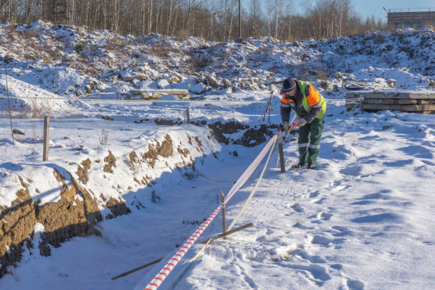 A worker at a construction site shields trenches with a signal tape for cadastral surveying.