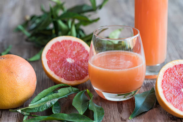 Healthy organic grapefruit juice surrounded by citrus leaves A glass of fresh, healthy organic grapefruit juice on a wooden table. There is a bottle of the grapefruit juice in the background. A halved pink grapefruit and citrus leaves are surrounding the drink. grapefruit photos stock pictures, royalty-free photos & images