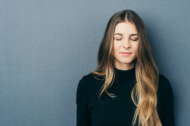Woman with eyes closed by wall with copy space Young long-haired woman with eyes closed standing against wall with copy space eyes closed stock pictures, royalty-free photos & images