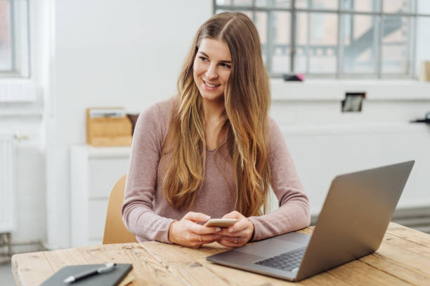 istock Young smiling woman using phone in front of laptop 1077969770