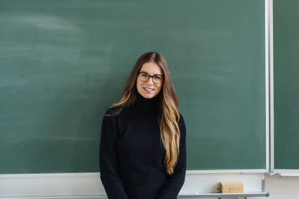 istock Young female teacher standing against blackboard 1077973148