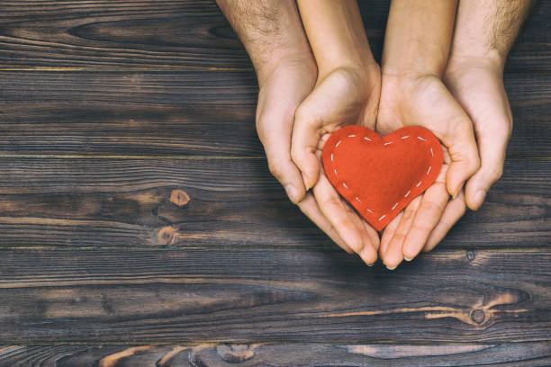 amour, notion de famille. gros plan des mains d’homme et une femme tenant à coeur de caoutchouc rouge ensemble tonique, vintage - heart shape human hand charity and relief work giving photos et images de collection