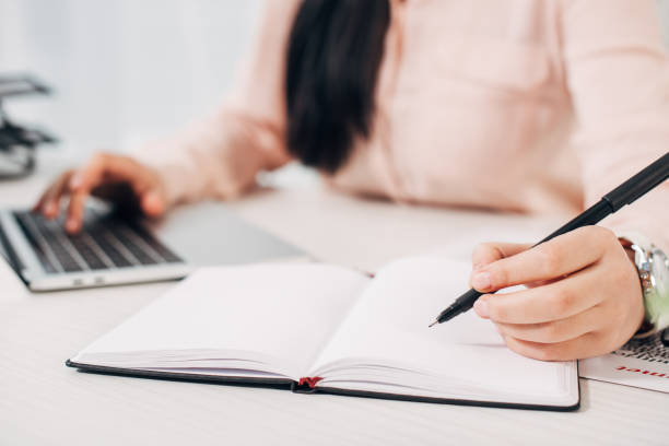 istock Cropped view of woman writing in notebook and typing on computer keyboard 1077982548