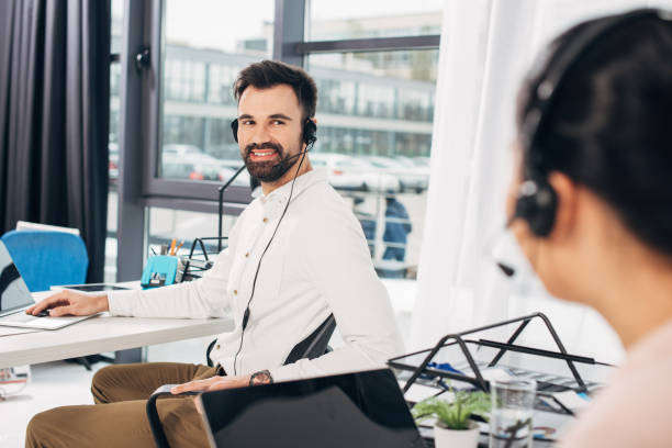 istock handsome call center operator smiling and looking to colleague in office 1077982632