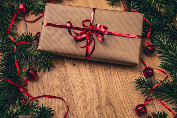 istock Christmas present on wooden board with fir tree, red bells. 1077984904