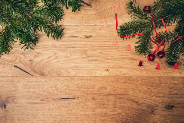 Christmas background with fir tree, red shiny bells on brown wooden table. Top flat view with copy space.
