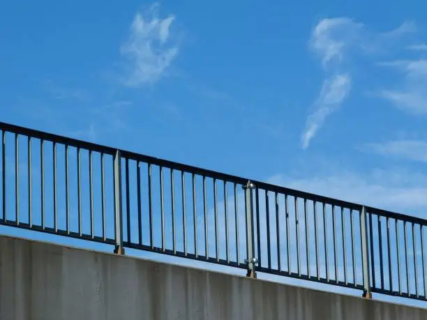 steel light guard rail along highway road in perspective view from below with blue sky above with vertical pickets and horizontal top rail and concrete slab below