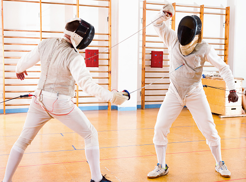 Portrait of glad cheerful positive smiling athletes at fencing workout, practicing attack movements in duel