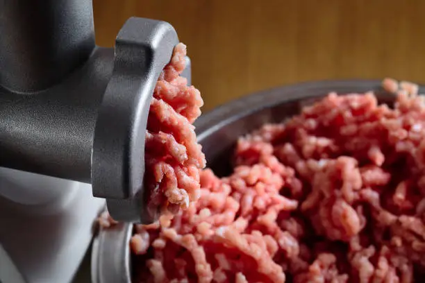 Minced fresh meat coming out from modern electric grinder on oak table as background. Healthy fresh homemade minced meat. Place for copyspace.