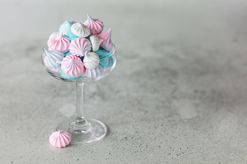 Homemade pastel pink, blue and white meringue in glass on neutral grey background. Horizontal minimalistic composition