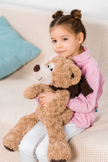 istock adorable child sitting on couch with teddy bear and smiling at camera 1078027460