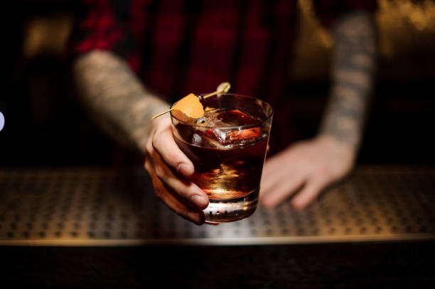 Professional bartender serving a delicious Godfather cocktail Professional bartender serving a delicious Godfather cocktail decorated with orange zest on the bar counter on the blurred background godfather godparent stock pictures, royalty-free photos & images