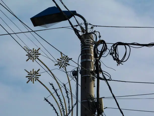abstract electrical utility light pole with decorative Christmas lighting with many connecting cables and wires under blue sky