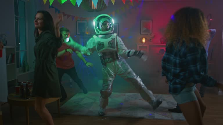 At the College House Costume Party: Fun Guy Wearing Space Suit Dances Off, Doing Groovy Funky Robot Dance Modern Moves. With Him Beautiful Girls and Boys Dancing in Neon Lights.