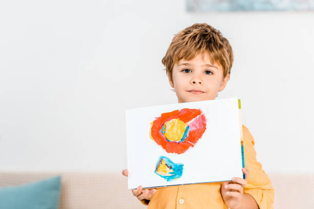 istock adorable little boy holding picture and looking at camera 1078051264